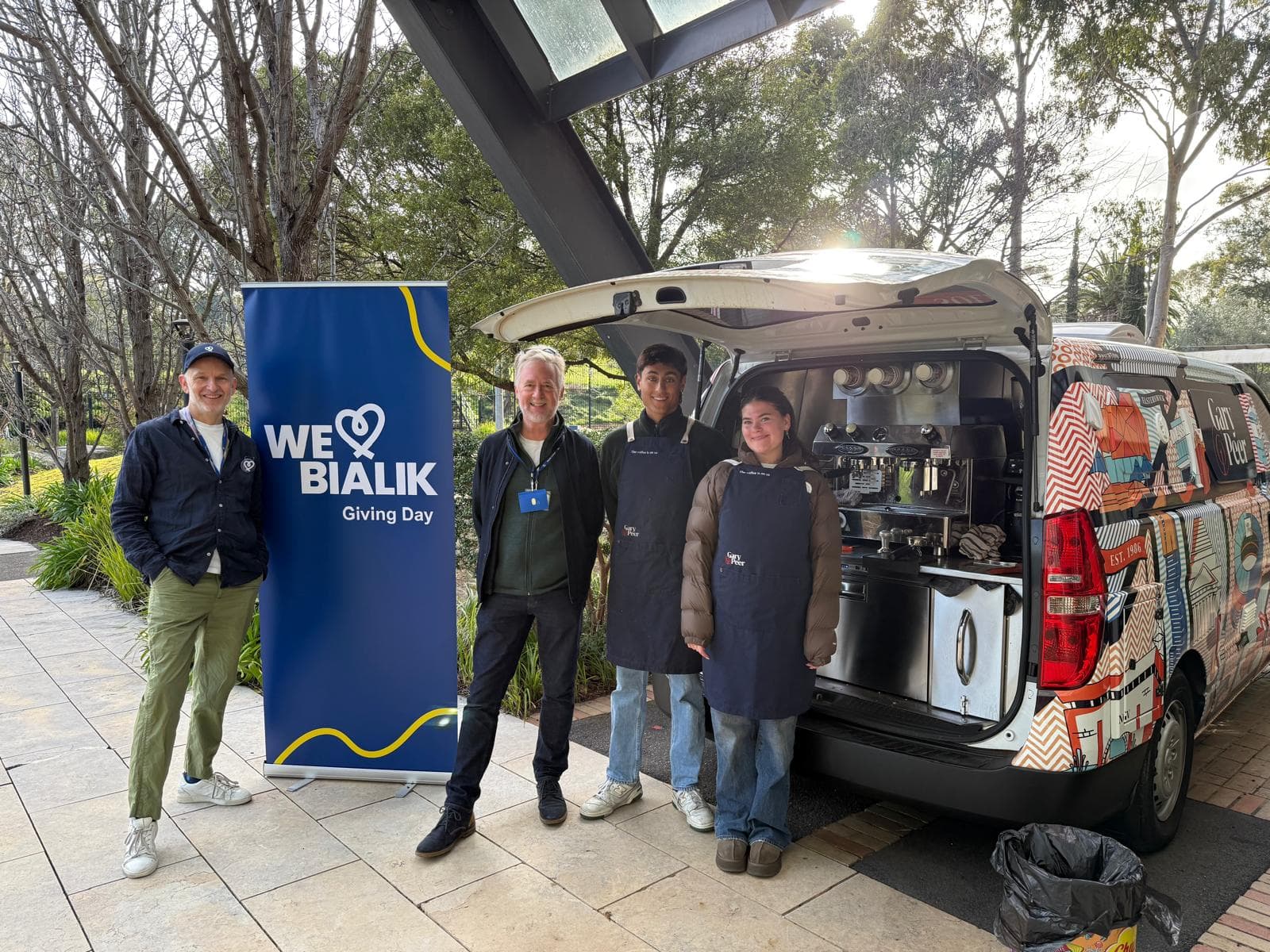 Staff and student volunteers beside the Giving Day coffee cart and We Love Bialik banner