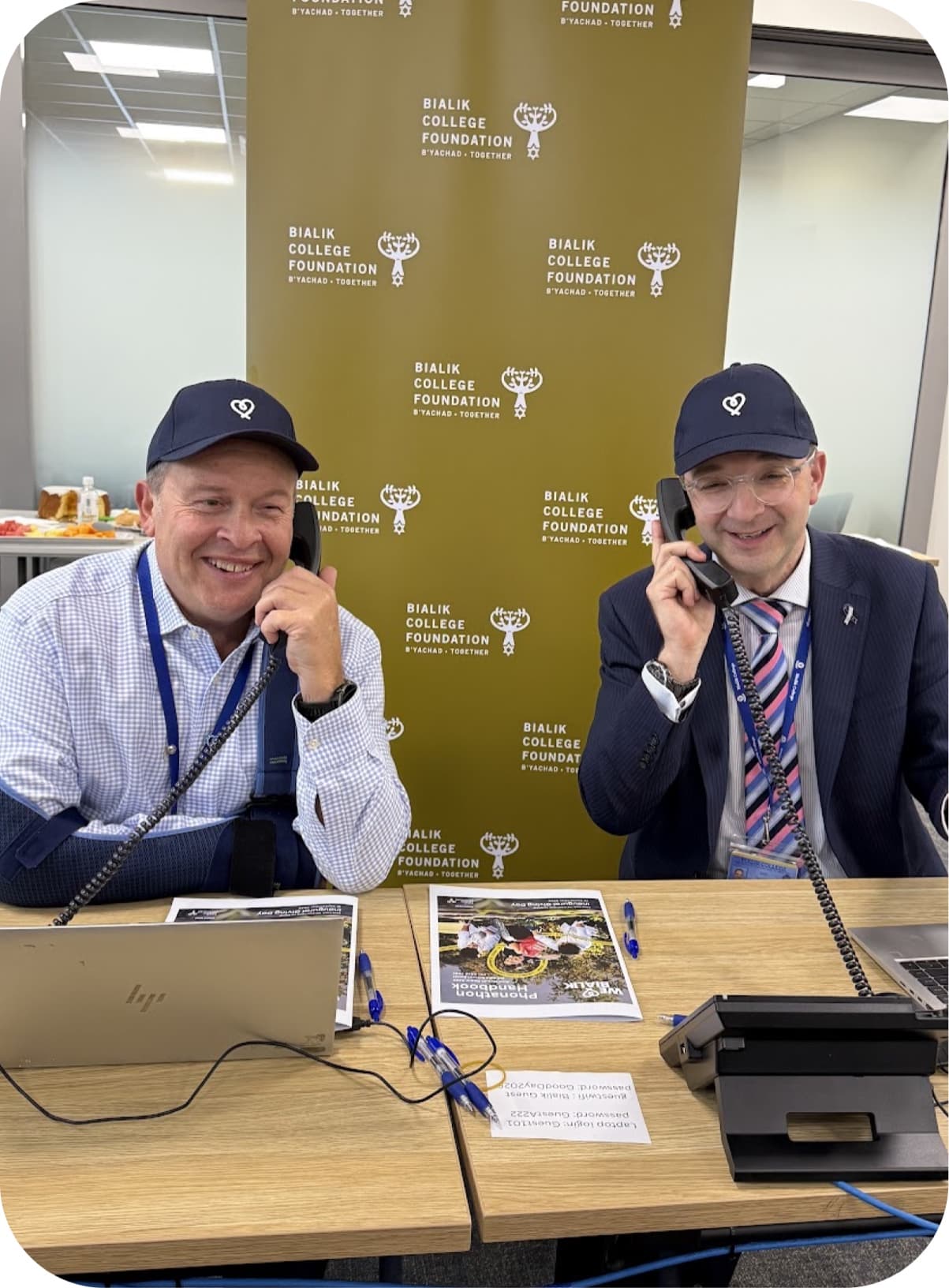 Two callers on the phones in front of a Bialik College Foundation banner